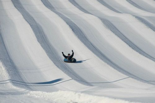 A person joyfully sledding down a snowy slope, arms raised, with wavy patterns in the snow.