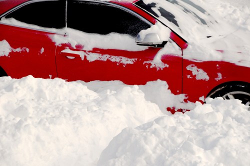 A red car partially buried in deep snow, with only the top and windows visible above the snowdrifts.