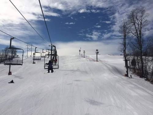 A snowy ski slope with chairlifts and a clear blue sky in the background.