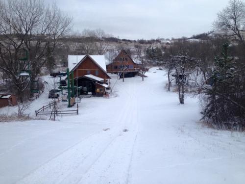 A snowy landscape featuring a rustic cabin and trees, with a path leading through the winter scenery.