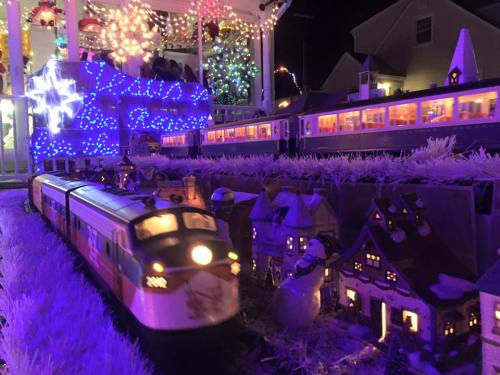 A festive train set with colorful lights, passing by miniature houses and a snowy landscape during the night.