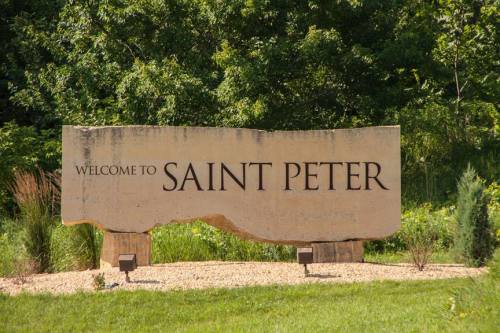Welcome sign for Saint Peter, featuring large text on a stone structure surrounded by greenery.