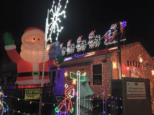 A festive house decorated with colorful Christmas lights, featuring a large inflatable Santa and reindeer on the roof.