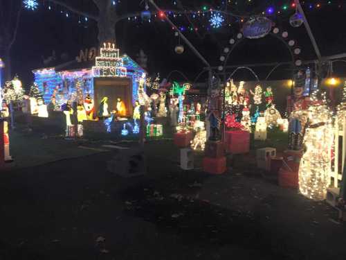 A festive display of colorful Christmas lights and decorations, featuring various holiday figures and a decorated house.