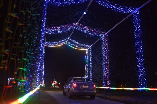 A car drives through a tunnel of colorful holiday lights at night, creating a festive atmosphere.