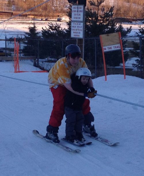 A person teaches a child to ski on a snowy slope, both wearing helmets and enjoying the winter activity.