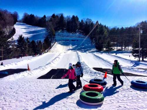 A snowy hill with people walking up, carrying colorful snow tubes, and others sliding down in the background.