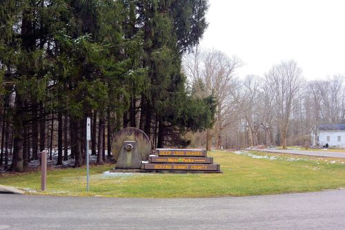 Sign for Deep Lock Quarry Metro Parks, surrounded by trees and grass, with a path leading into the park.