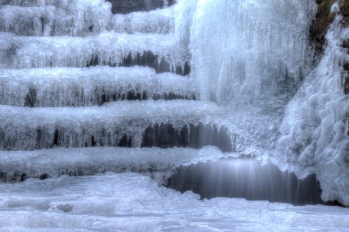 Frozen waterfall with icy steps and cascading water, creating a serene winter landscape.