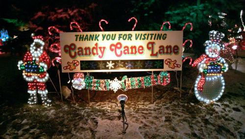 A festive sign reading "Thank You for Visiting Candy Cane Lane," surrounded by holiday lights and decorations.