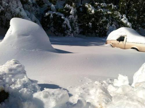 A snowy landscape with two partially buried vehicles and a thick blanket of snow covering the ground.