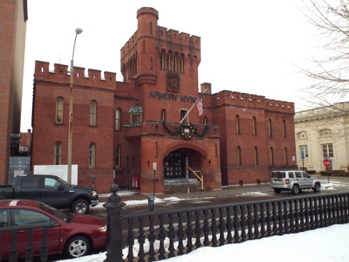 Historic red brick building with a castle-like design, featuring an American flag and holiday wreath on the entrance.