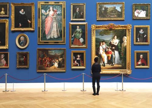 A person stands in front of a gallery wall adorned with various framed paintings and portraits.