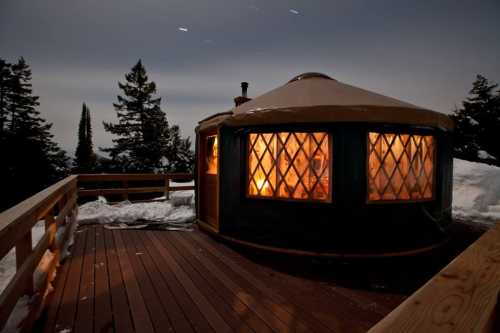 A cozy yurt with glowing windows, surrounded by snow and trees, under a starry night sky.