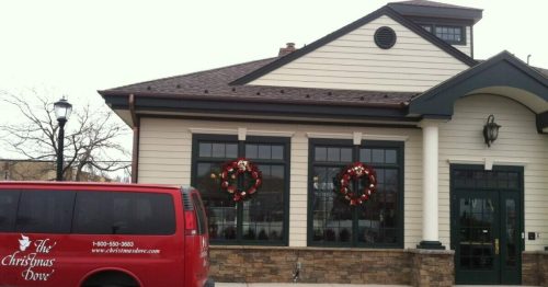 A red van parked outside a building decorated with holiday wreaths on the windows.