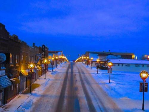 A snowy street lined with lamp posts, buildings, and a twilight sky, creating a serene winter scene.