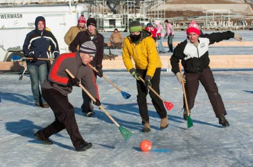 A group of people playing a game on ice, using brooms to hit a ball, dressed in winter clothing.