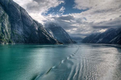 A serene fjord with towering mountains and calm turquoise waters under a cloudy sky.