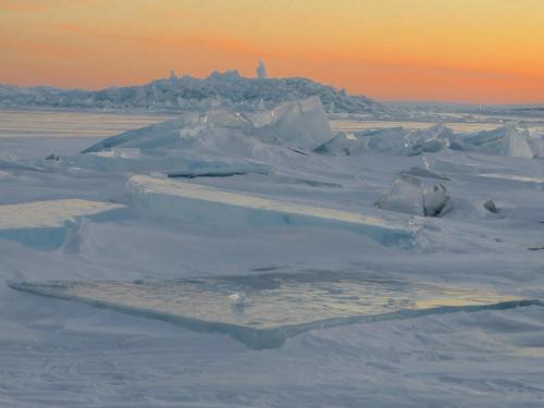 Ice formations on a frozen landscape with a soft sunset glow in the background.