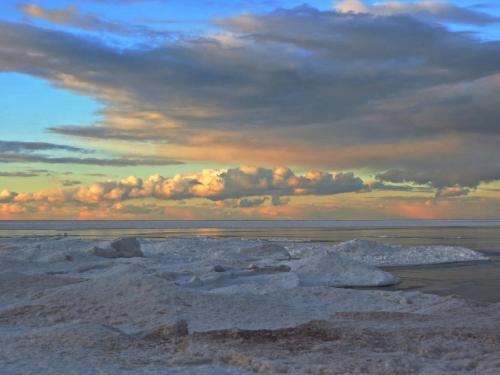 A serene seascape at sunset, featuring soft clouds and ice formations along the shoreline.