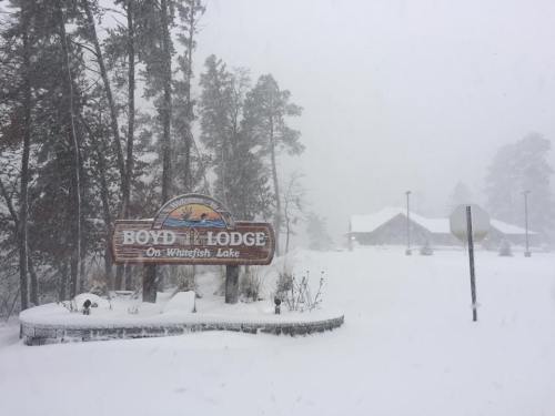 Sign for Boyd Lodge on Whitefish Lake, surrounded by heavy snowfall and trees, with a lodge visible in the background.