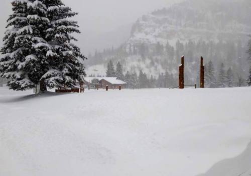 A snowy landscape with a cabin and trees, surrounded by deep snow and a misty mountain backdrop.
