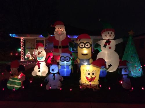 Colorful inflatable holiday decorations, including Santa, snowmen, and a Minion, illuminated in a festive yard display.