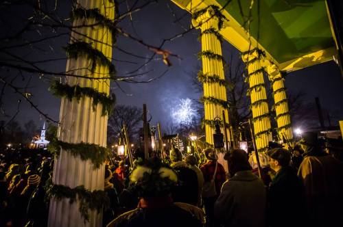 Crowd gathered under columns, watching fireworks illuminate the night sky during a festive event.