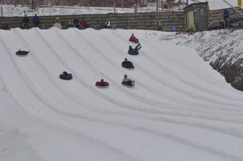 A snowy hill with several people tubing down, enjoying a winter day. Snow-covered slopes and a snowy landscape in the background.