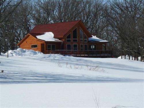 A wooden house with a red roof surrounded by snow and trees on a winter day.