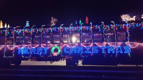 A brightly lit train decorated with colorful Christmas lights and a "Merry Christmas" sign.