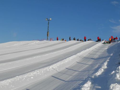 A snowy hill with people sledding and a ski lift in the background under a clear blue sky.