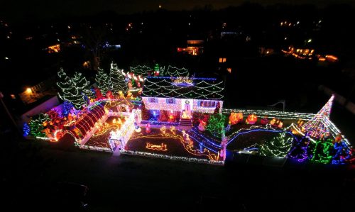 Aerial view of a brightly lit house and yard decorated with colorful Christmas lights and festive displays at night.