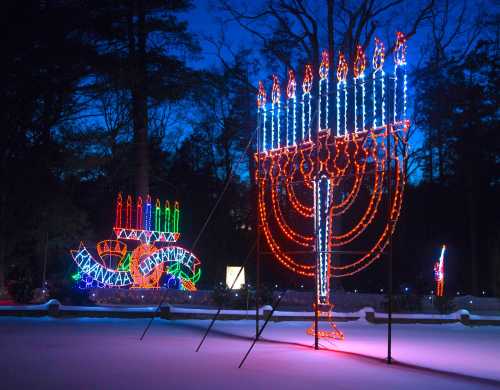 Colorful holiday lights display featuring a large menorah and a smaller dreidel, set against a twilight sky.