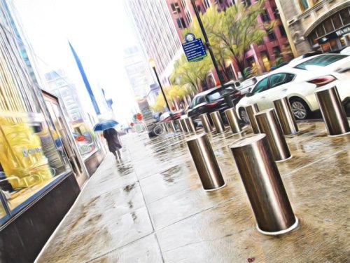 A rainy city street with a person holding an umbrella, lined with metallic bollards and buildings in the background.