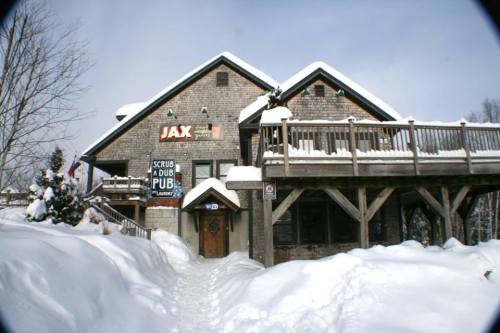 A snowy scene of a rustic building with a sign for "Jax Scrub a Dub Pub," surrounded by winter landscape.