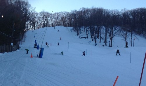Skiers and snowboarders navigate a snowy slope surrounded by trees at a winter sports area.