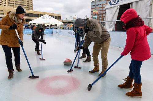 A group of people curling on an ice rink, focused on their stones and using brooms to guide them.