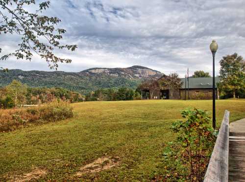 Scenic view of a grassy field with a log cabin and mountains under a cloudy sky.