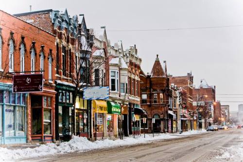 A snowy street lined with historic brick buildings and shops, creating a charming winter scene.