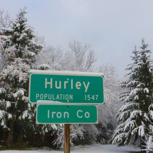 Sign for Hurley, Iron County, with snowy trees in the background. Population listed as 1,547.