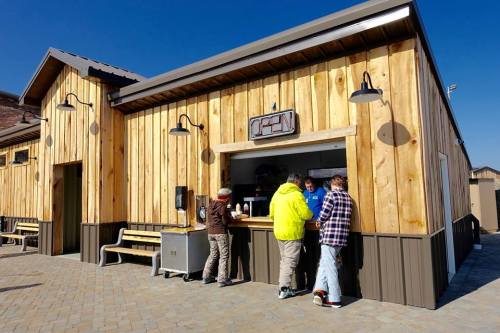 A wooden building with a sign reading "OPEN," where people are ordering at a counter on a sunny day.
