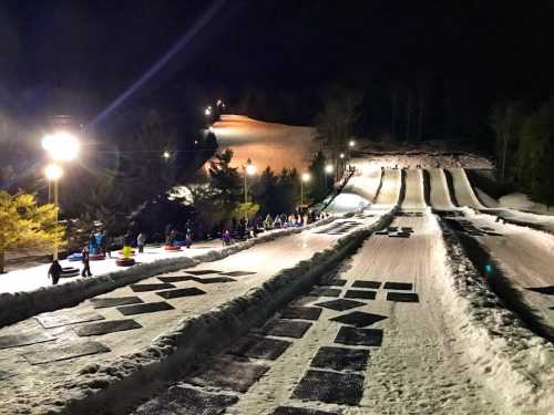 Nighttime view of a snow tubing hill with illuminated lanes and people enjoying the winter activity.