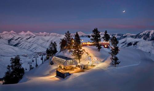 A snowy mountain landscape at dusk, featuring a cozy lodge and illuminated pathways among pine trees.