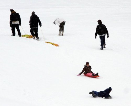 People sledding and playing in the snow, with some walking in the background on a snowy landscape.