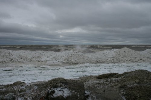 A turbulent sea with frothy waves under a cloudy sky, creating a dramatic coastal scene.