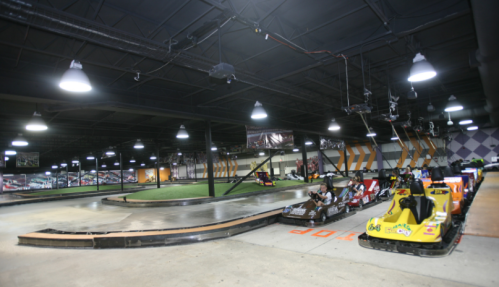 Indoor go-kart track with several karts lined up and a winding track under bright lights.