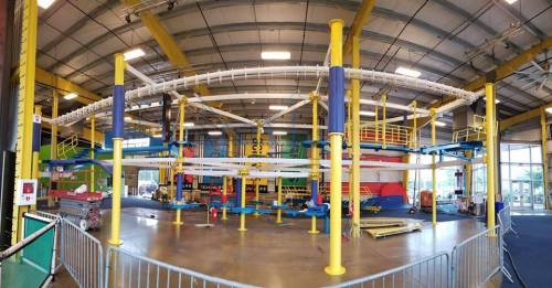 Indoor adventure park featuring colorful climbing structures and obstacle courses under a high ceiling.