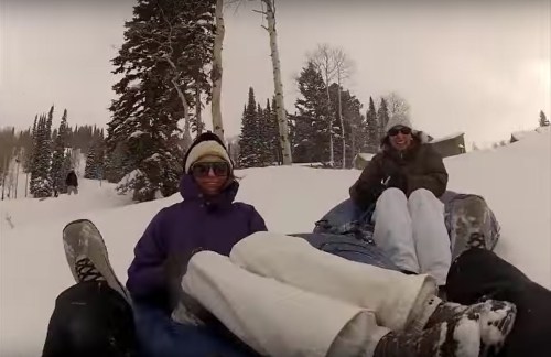 A group of friends enjoying a snow tubing adventure on a snowy hillside, surrounded by tall trees.