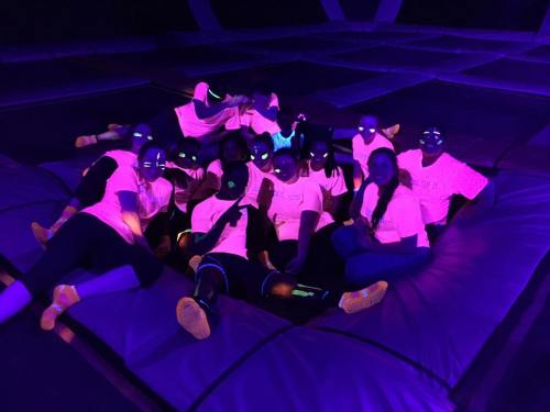 A group of people in neon shirts poses together under blacklight, creating a vibrant, glowing effect.